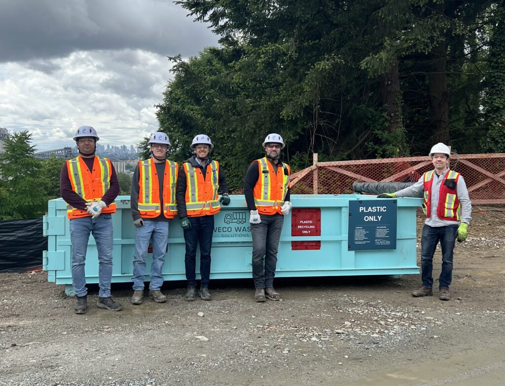 A group of construction workers in front of a designated plastics-only recycling bin.